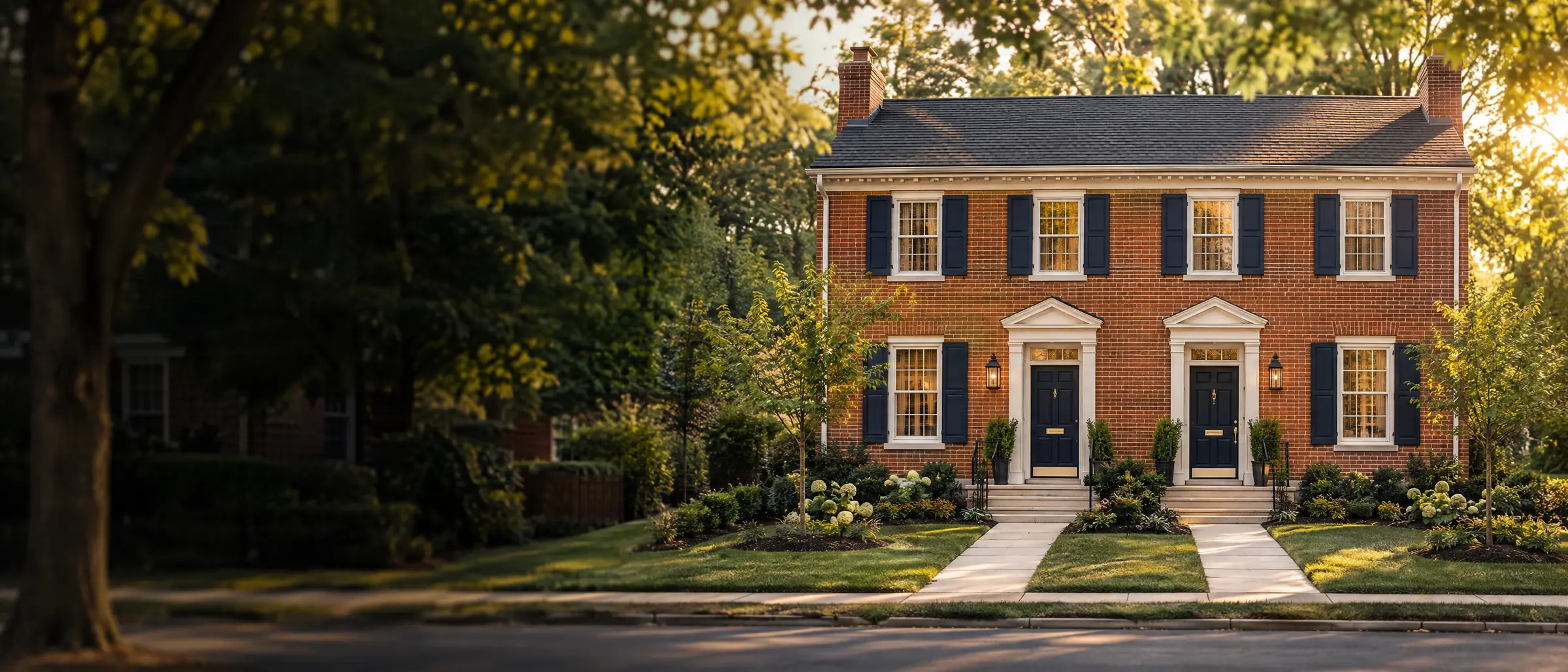 A renovated brick duplex with navy doors and shutters on a tree-lined street