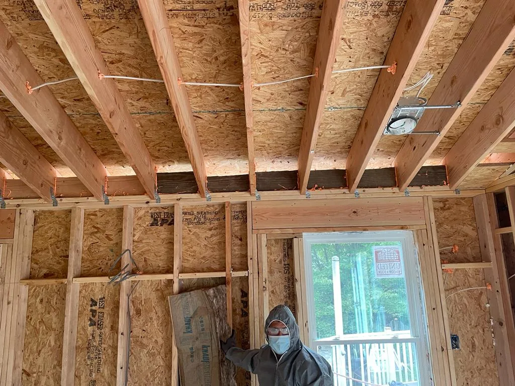 An interior stripped to its framing, showing new ceiling joists and stud walls, with a worker at the far end.