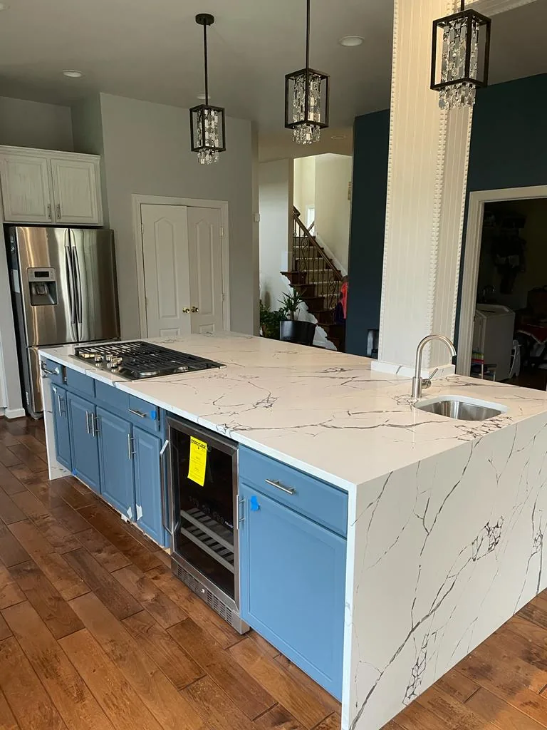 A remodelled kitchen with deep blue base cabinets, a thick white quartz island with grey veining, stainless appliances and hardwood floors.
