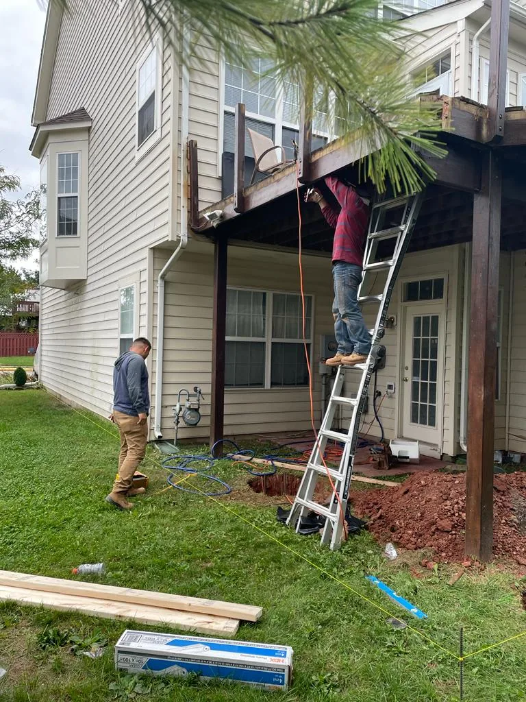 Two workers, one on a ladder, replacing siding and trim on the upper storey of a house.